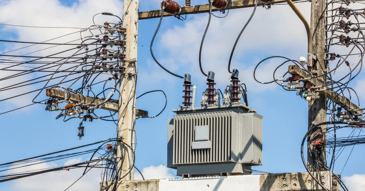 Electrical transformer and power lines mounted on utility poles against a blue sky